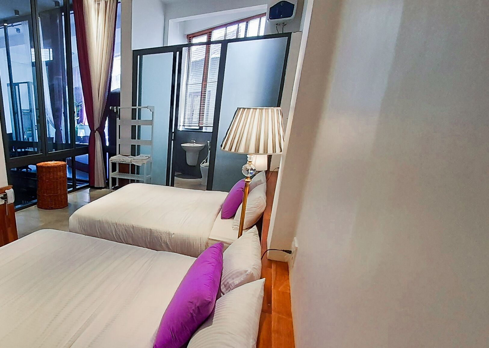 Une chambre d’hôtel avec deux lits, une fenêtre avec des stores, une lampe et une vue sur l’extérieur.