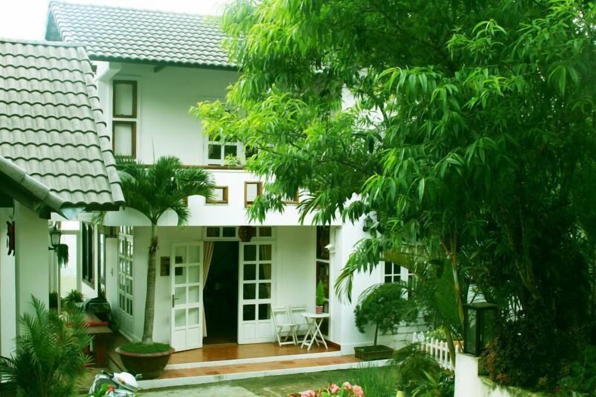 A white house with a tiled roof, a covered porch, and a small garden with potted plants and a fountain.