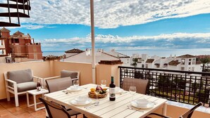 A terrace with a table set for two, overlooking a coastal cityscape. - Duquesa Regent Penthouse 2435 Sea-view Duplex (Manilva)
