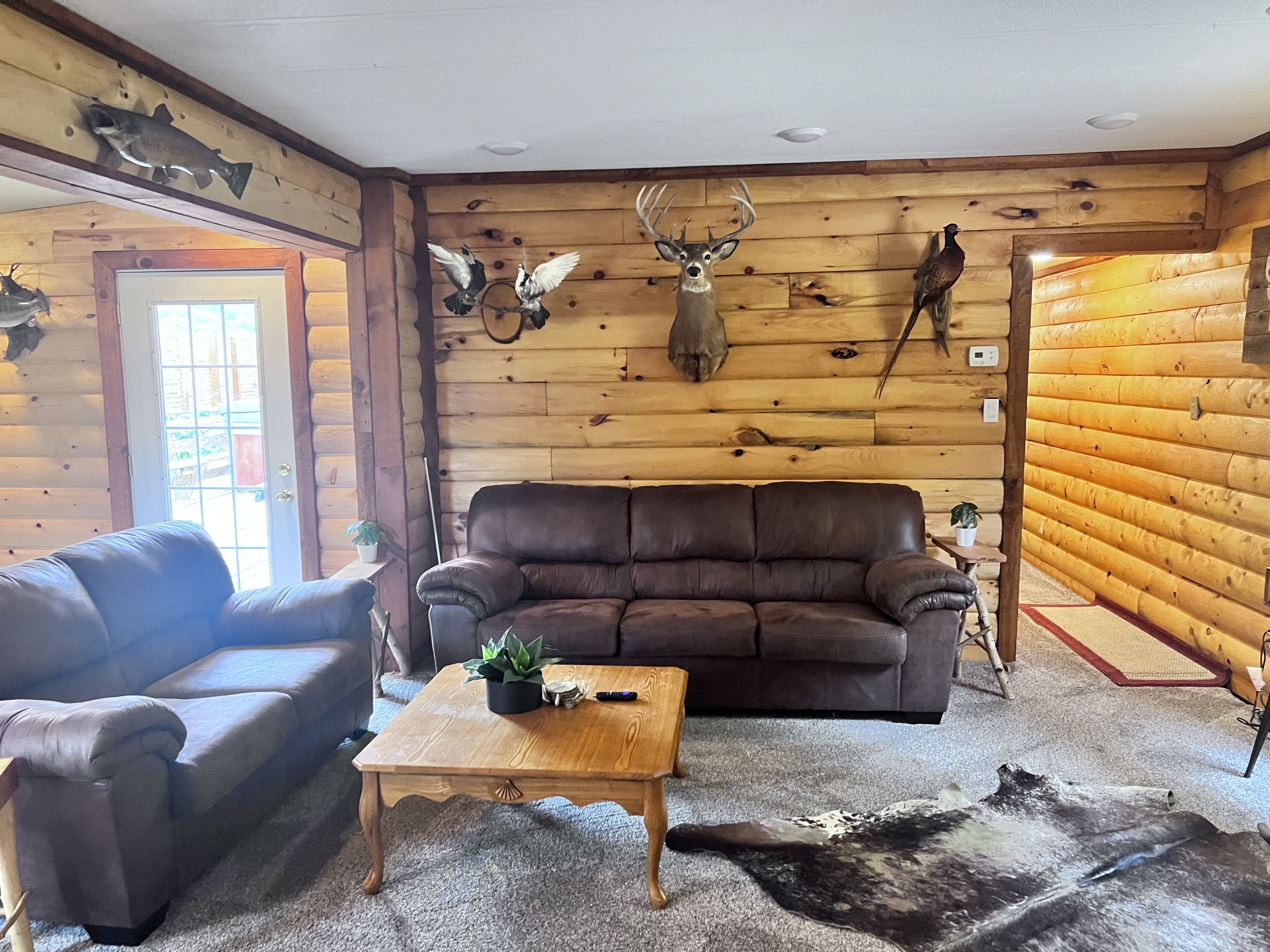 A log cabin interior with a brown leather sofa, a wooden coffee table, and a rug.