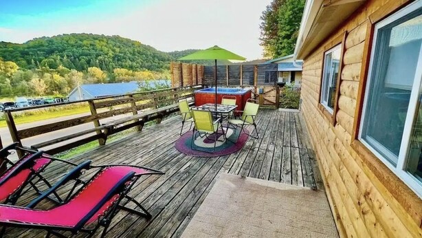 Eine Holzterrasse mit Tisch und Stühlen, ein rotes Liegestuhl und Blick auf eine bewaldete Landschaft.