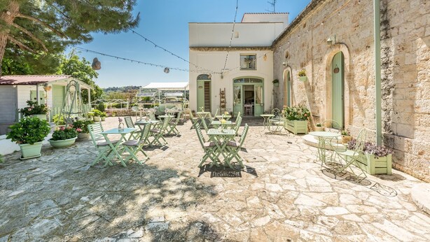 Un patio con mobiliario exterior, suelo de piedra y un edificio con ventanas arqueadas.