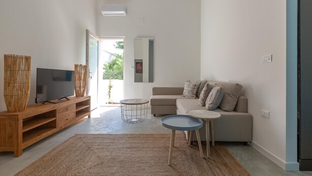 A modern living room with a TV on a wooden stand, a beige sofa, two small tables, and a large woven rug. - 3321 Villa Fiorezza - App 4 by Barbarhouse (Maruggio)