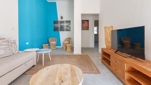 A modern living room with a blue accent wall, a large flat-screen TV, a sofa, a coffee table, and wicker chairs. - 3321 Villa Fiorezza - App 4 by Barbarhouse (Maruggio)