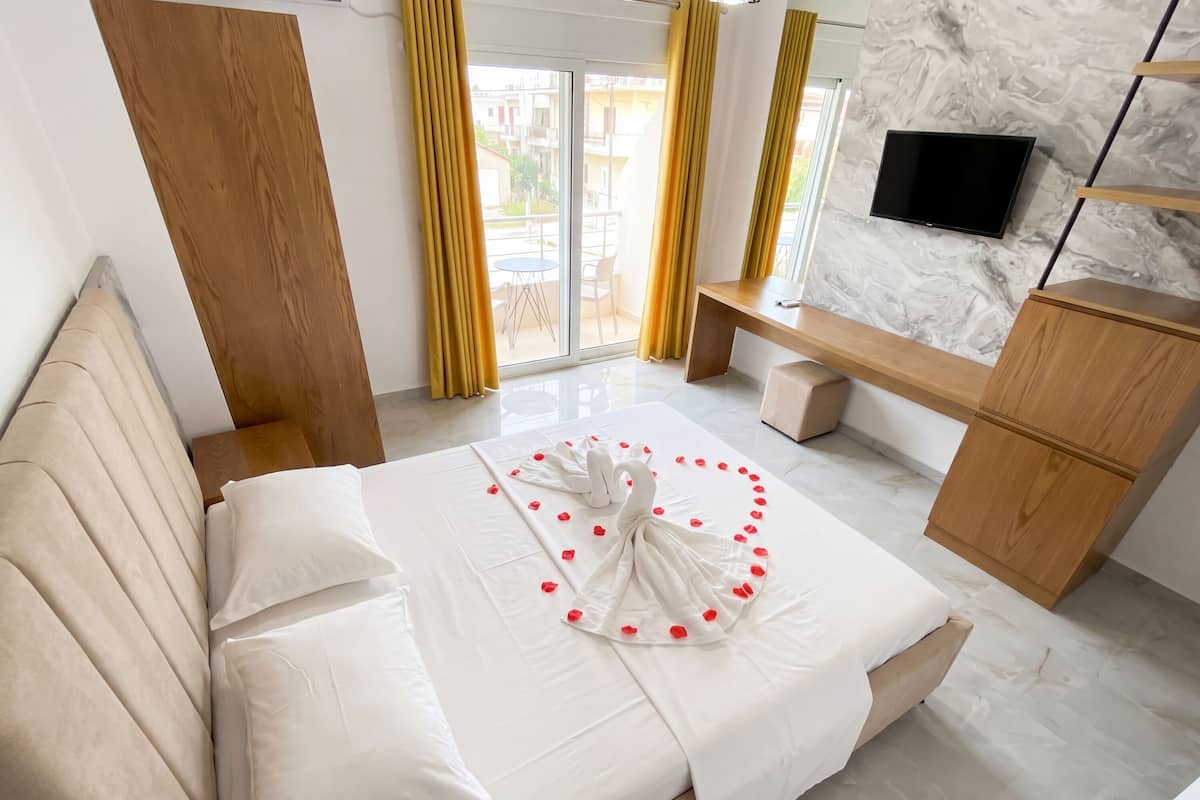 A hotel room with a bed, a TV, a wooden bench, and a marble wall.
