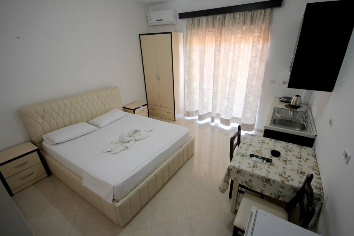 A bedroom with a bed, bedside tables, a wardrobe, a desk with a chair, and a window with curtains.