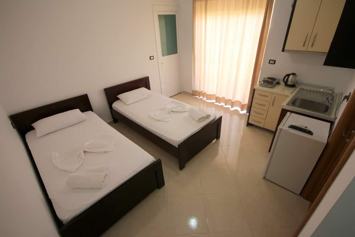A hotel room with two beds, a kitchenette, and a bathroom.