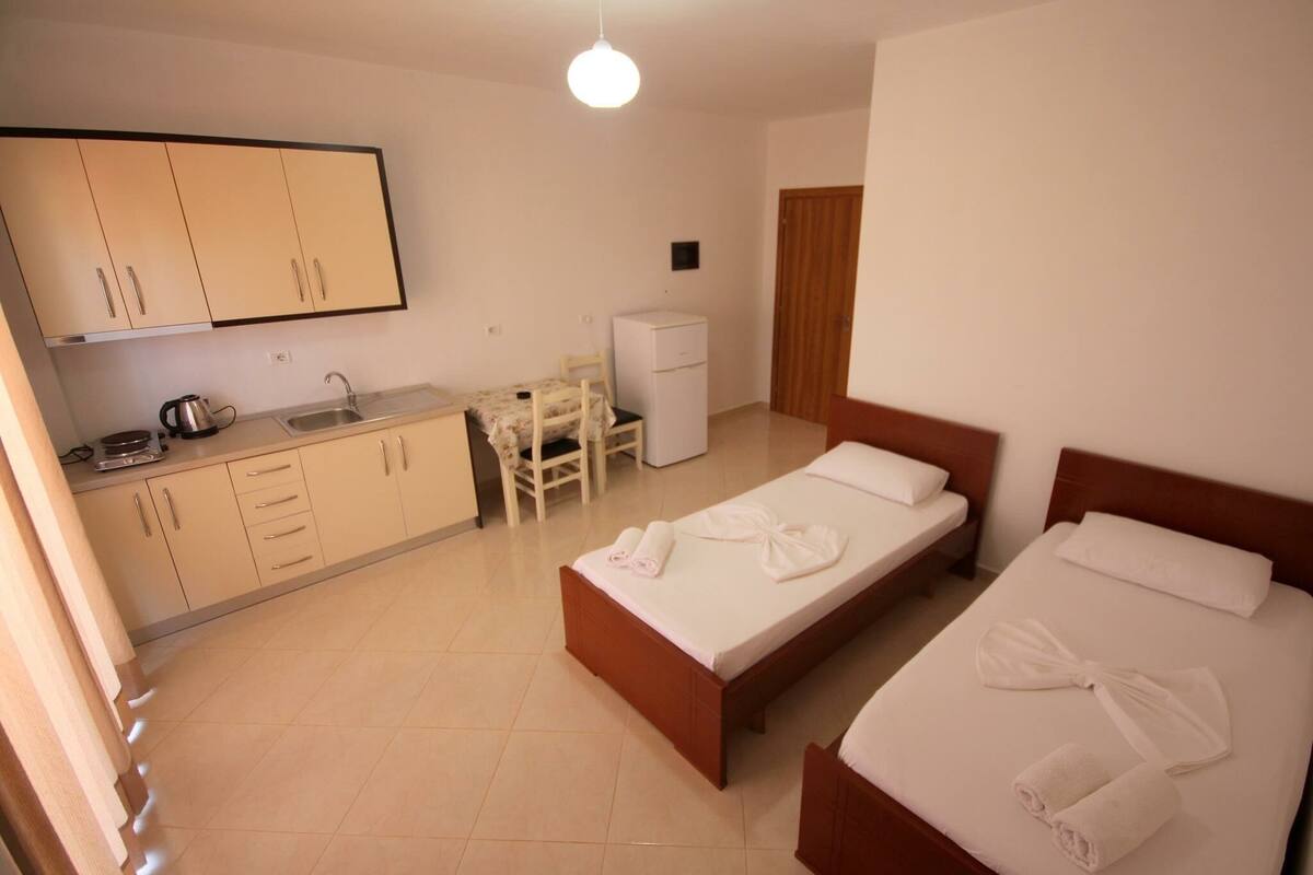 A hotel room with two beds, a small kitchenette, a desk, and a refrigerator.