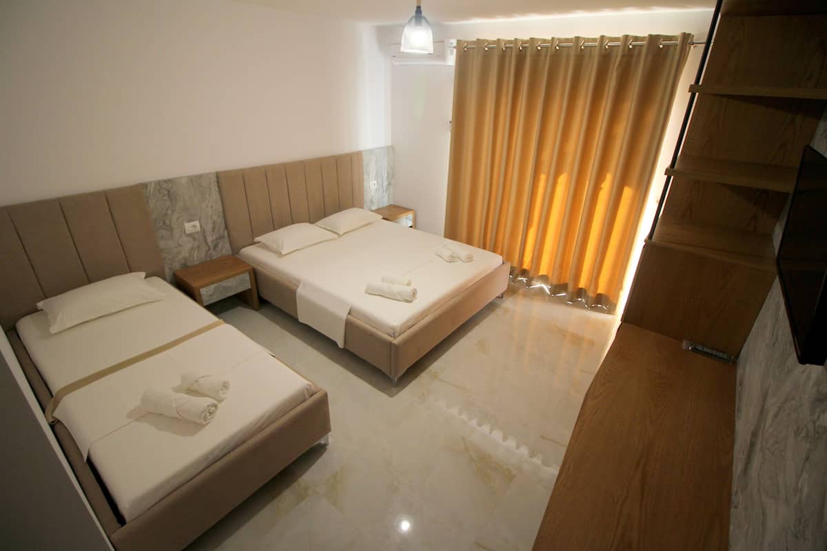 A hotel room with two beds, a nightstand, a lamp, and a window with curtains.