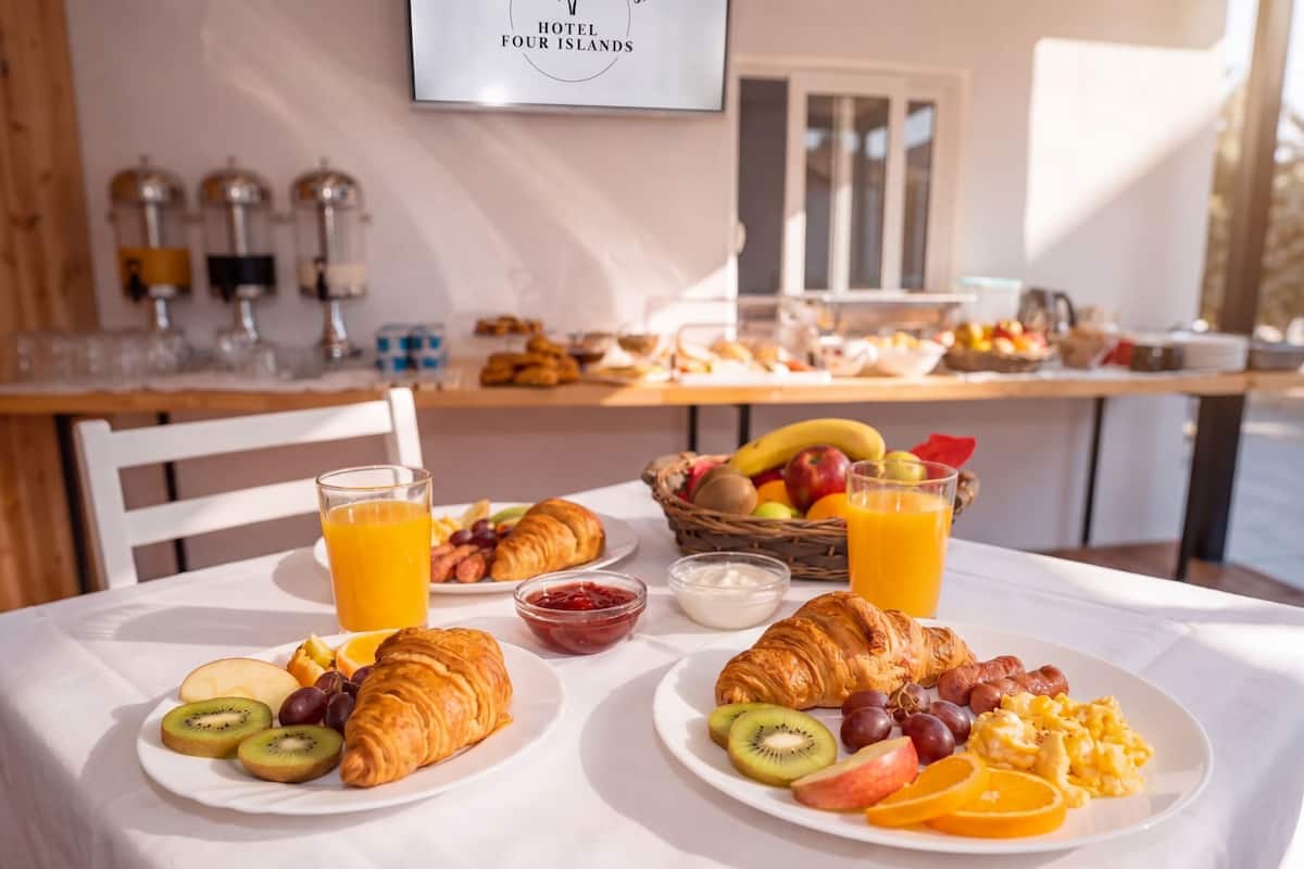 Breakfast plates with fruits, croissants, and orange juice on a table in a hotel dining area.