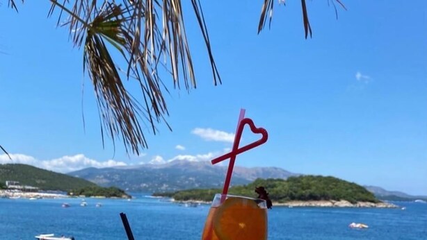A beach scene with a clear view of the sea, beach umbrellas, and lounge chairs. - Hotel Four Islands (Ksamil)