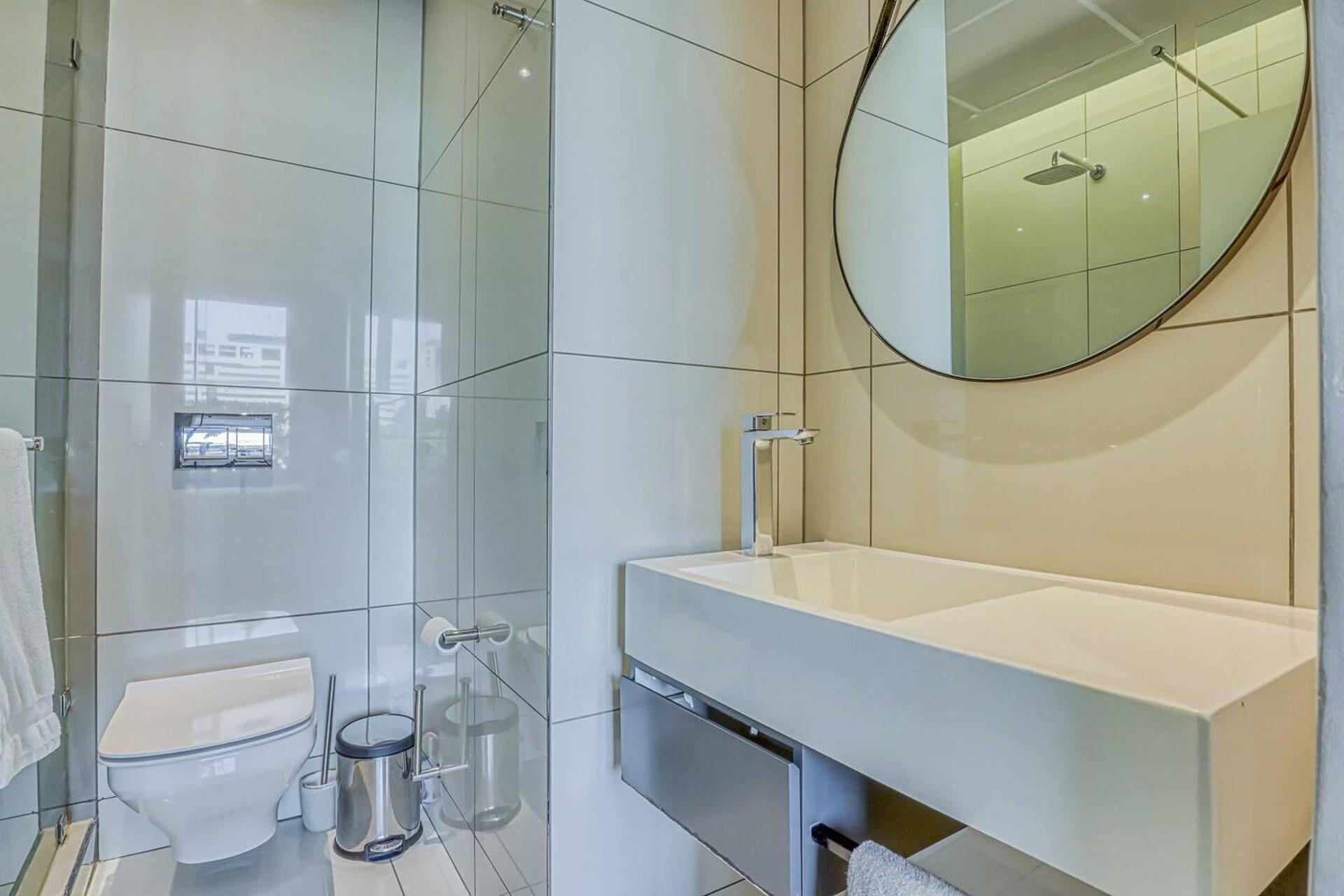 Ein modernes Badezimmer mit Duschkabine aus Glas, Toilette, Waschbecken mit Spiegel und Mülleimer.