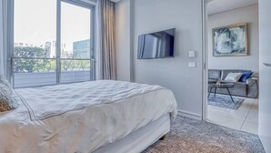 A modern bedroom with a large bed, a TV, and a balcony with a city view. - Luxury 1 Bed Apartment at The Capital on the Park (Johannesburg)