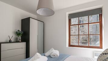 Un dormitorio con cama, armario, ventana con vista a edificios de piedra y lámpara colgante.