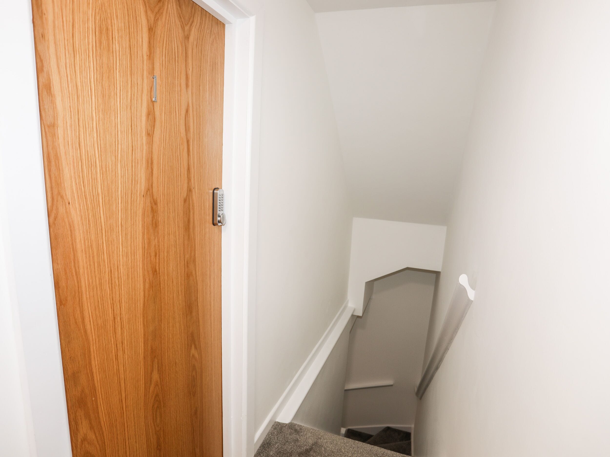 A wooden door with a keypad lock, a white wall, and a staircase leading to a landing.