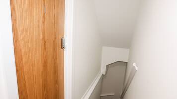 A wooden door with a keypad lock, a white wall, and a staircase leading to a landing.