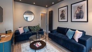 Een moderne woonkamer met twee donkerblauwe banken, een glazen salontafel en een ronde spiegel aan de muur.