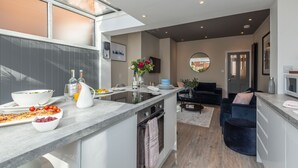 Een moderne keuken met een centraal eiland, een zithoek met een donkerblauwe bank, en een woonkamer met een ronde spiegel.