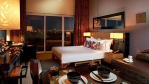Quarto de hotel com cama, mesas de cabeceira, escrivaninha e vista para a cidade à noite.