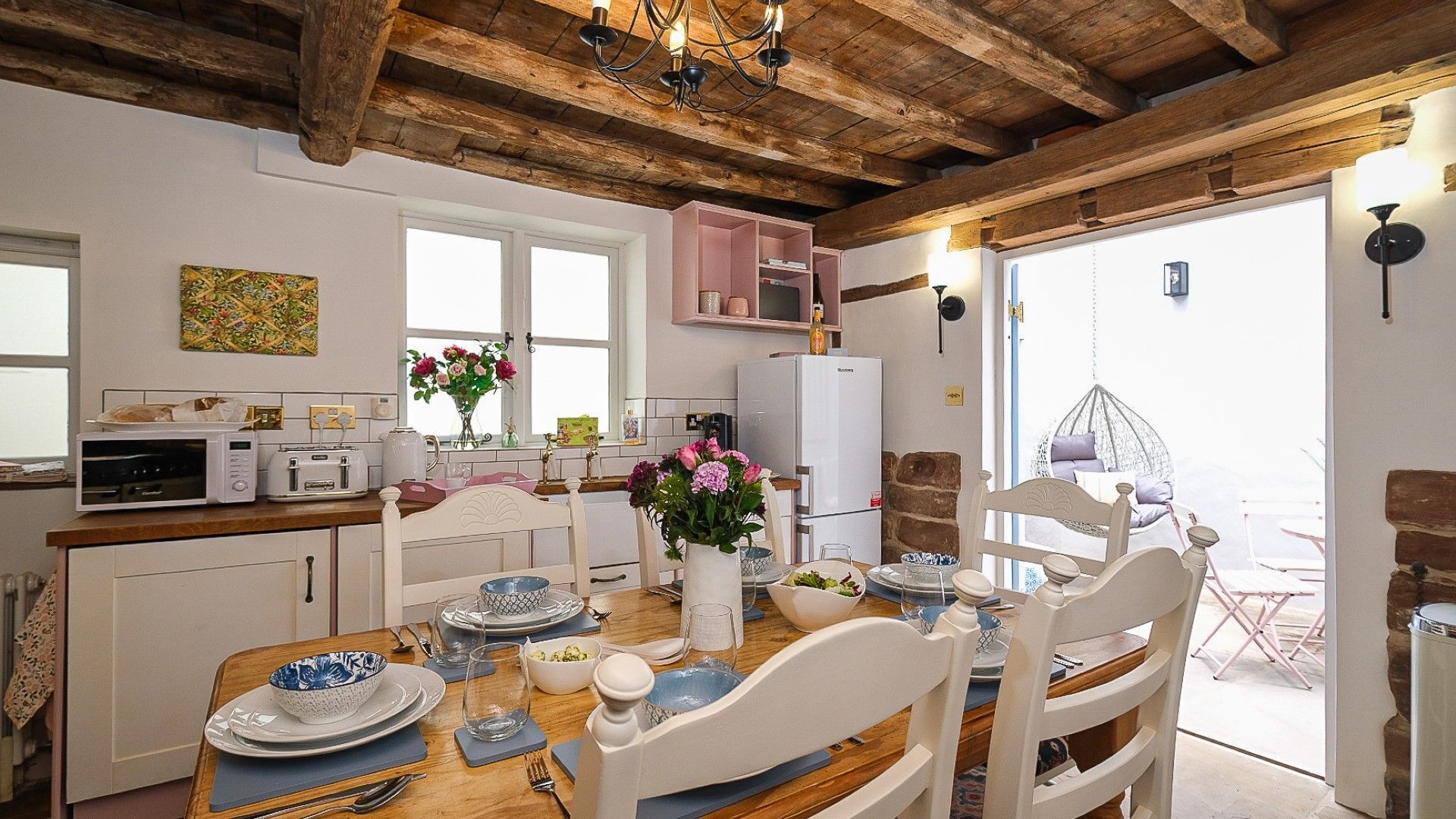 Een gezellige keuken met houten balken, een eetgedeelte met witte stoelen en een hangstoel buiten.