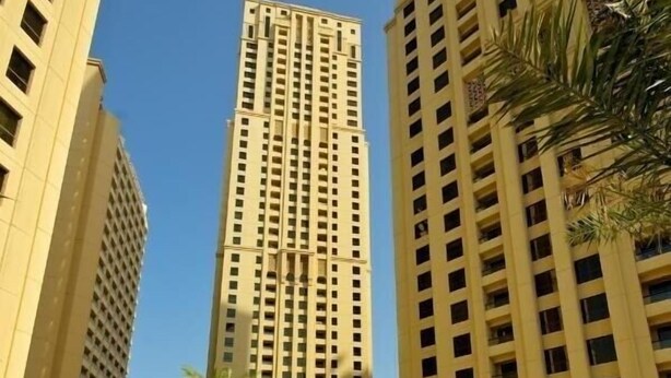 A swimming pool area with lounge chairs and palm trees, surrounded by tall buildings. - Three Bedroom Apartment In Sadaf 3 Jbr By E R (Dubai)