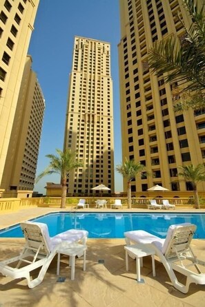 A swimming pool area with lounge chairs and palm trees, surrounded by tall buildings. - Three Bedroom Apartment In Sadaf 3 Jbr By E R (Dubai)