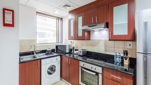 A compact kitchen with wooden cabinets, a washing machine, a microwave, a toaster, and a refrigerator. - One Bedroom Apartment In Sadaf 3 Jbr By E R (Dubai)