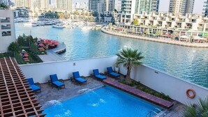 Una piscina en la azotea con sillones azules y vistas a un puerto deportivo con barcos.
