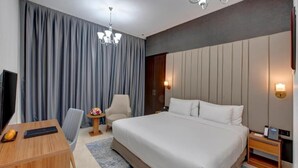A hotel room with a large bed, a desk, a chair, a TV, and a nightstand with a phone.