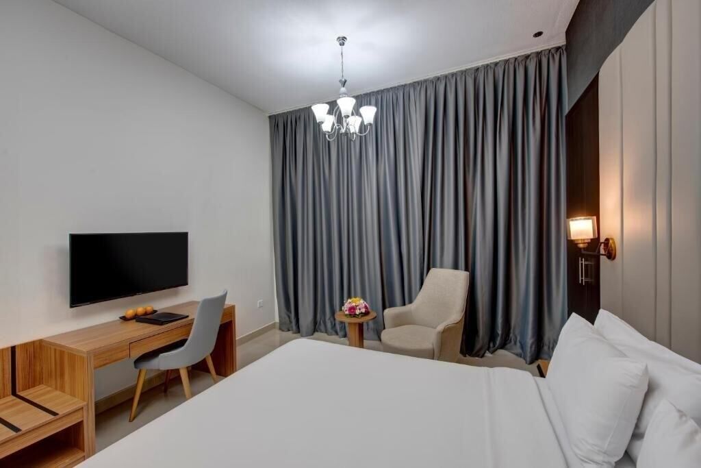 A modern hotel room with a large bed, a desk with a chair, a television, and a chandelier.