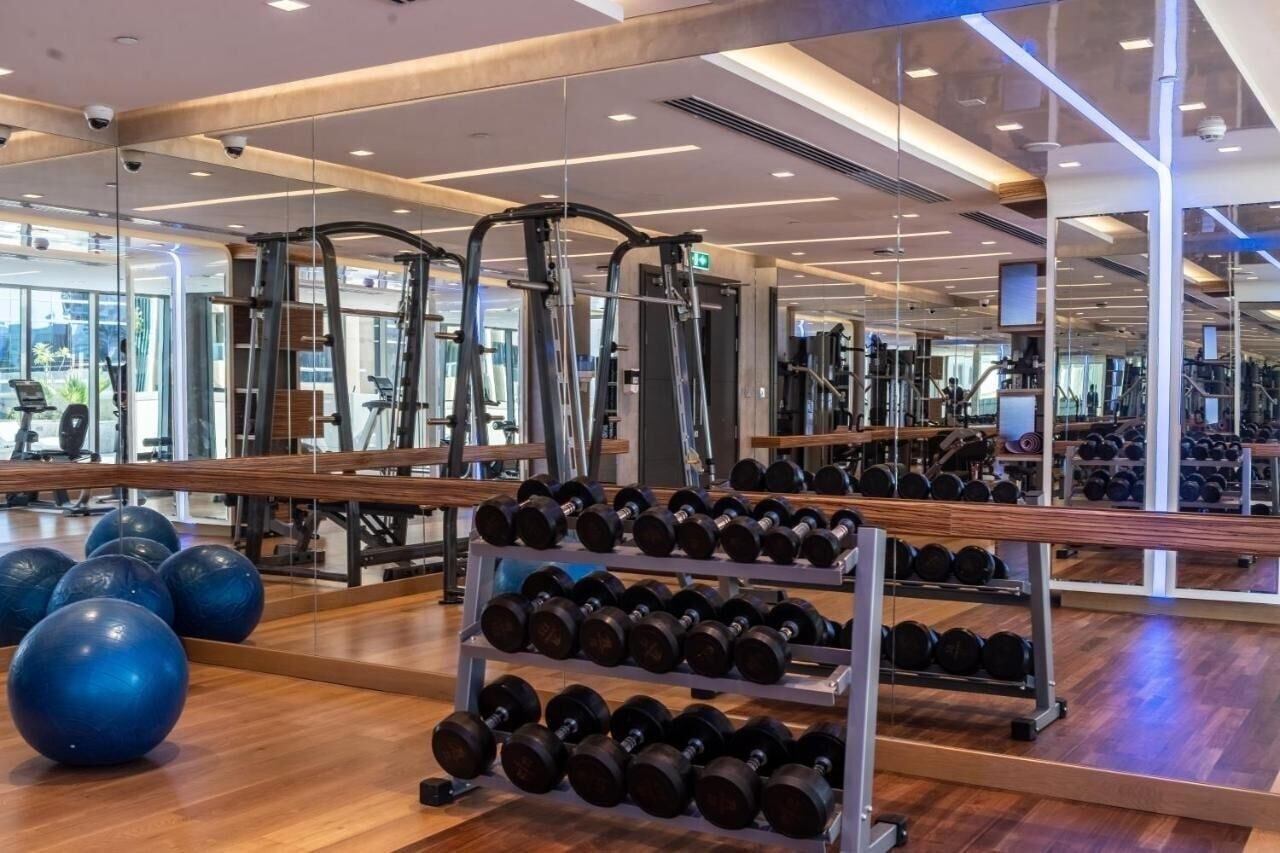 Un gimnasio con equipamiento de ejercicio, espejos y racks para pesas.