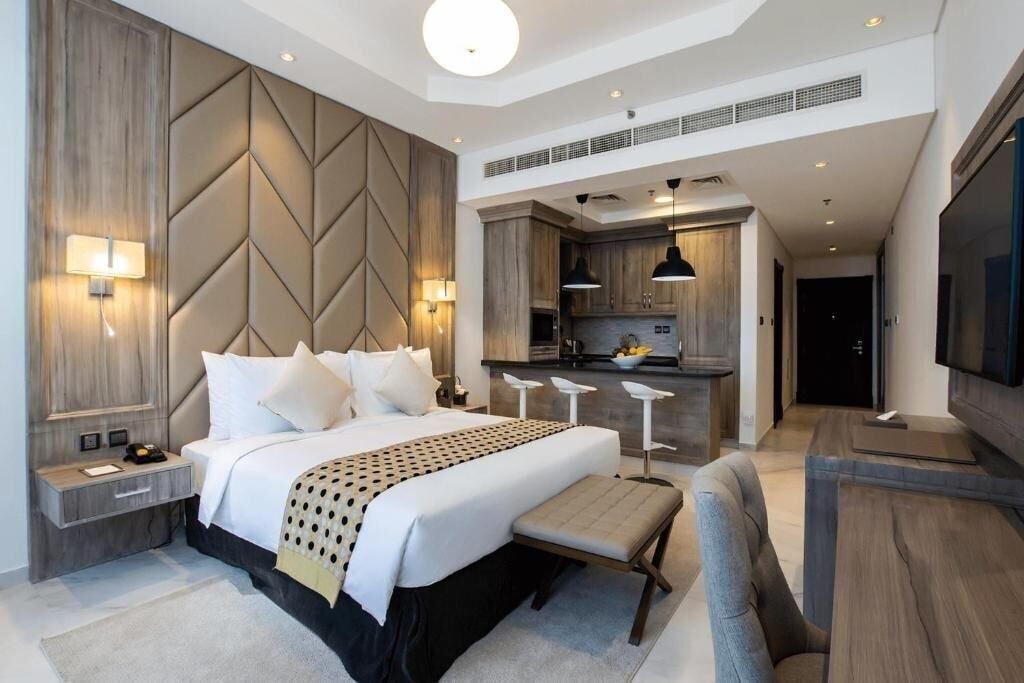 A modern hotel room with a large bed, a desk, and a kitchenette.