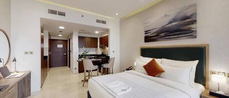 A hotel room with a large bed, a desk, and a kitchenette.