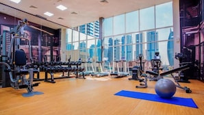Et fitnesscenter med træningsudstyr, store vinduer og udsigt over byen.