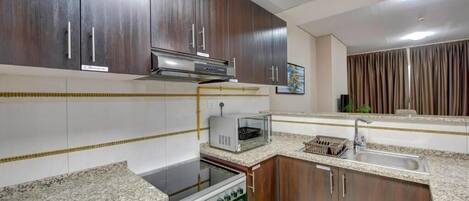 Una cocina compacta con armarios de madera oscura, horno empotrado, microondas y encimera de granito.