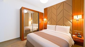 Een hotelkamer met een groot bed, een kledingkast met spiegel en wandlampen.