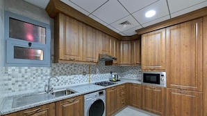 Een keuken met houten kastjes, een ingebouwde wasmachine, een magnetron en een betegelde spatwand.