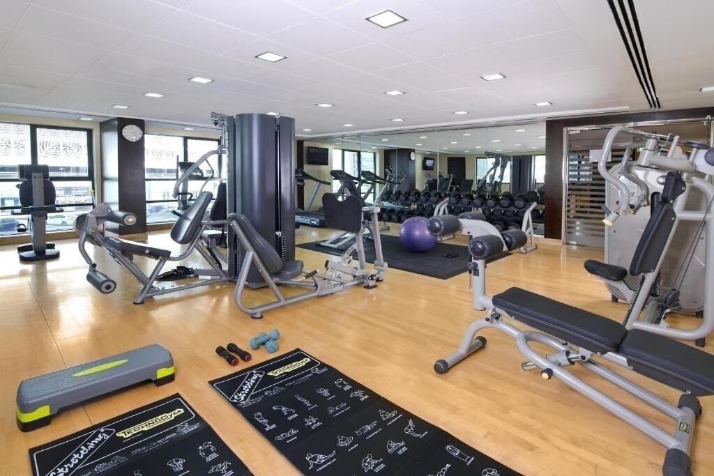 Un gimnasio con varios equipos de ejercicio, un espejo grande en la pared y piso de madera.