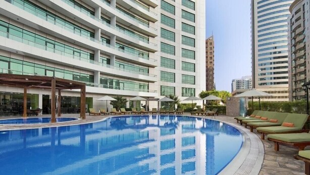 Una piscina con lettini e ombrelloni, circondata da edifici alti.