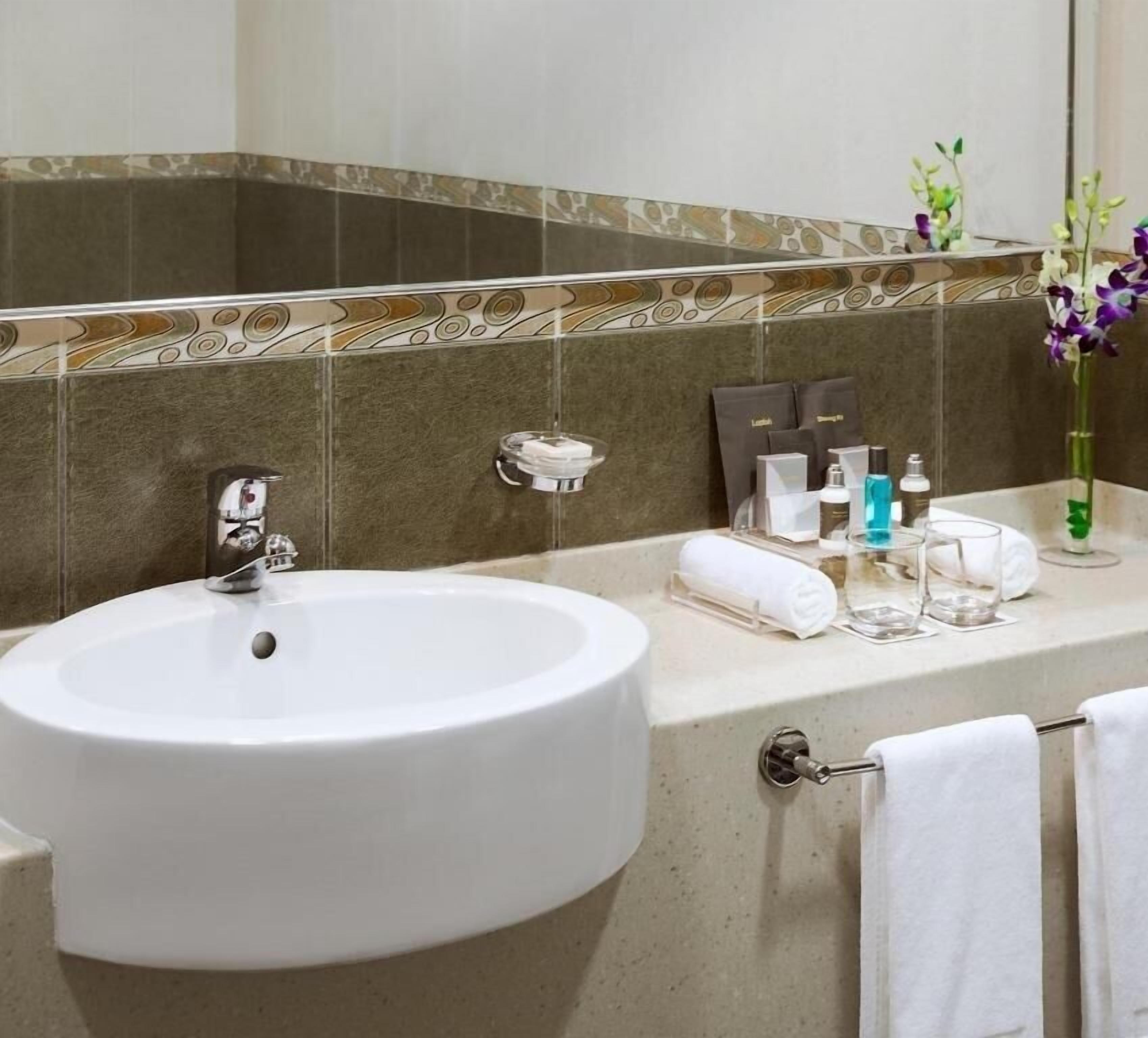 Une salle de bain avec un lavabo blanc, un porte-serviettes et des articles de toilette posés sur le comptoir.