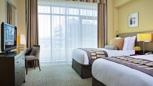 Una camera d'albergo con un letto grande, una scrivania con televisore, una sedia e una finestra con tende.