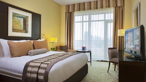 A hotel room with a large bed, a television, a desk with a lamp, and a chair.