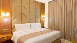 Une chambre d’hôtel avec un grand lit, une tête de lit en bois, deux tables de chevet et une grande fenêtre avec des rideaux.