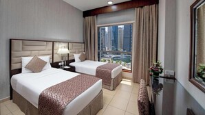 A hotel room with two beds, a large window with a city view, a desk with a lamp, and a small table with a vase of flowers. - Two Bedroom Apartment Marina view In Sadaf 3 (Dubai)