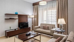 A modern living room with a flat-screen TV, sofa, coffee table, and a small side table with a lamp. - Two Bedroom Apartment Marina view In Sadaf 3 (Dubai)
