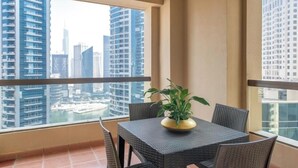 A balcony with a table and chairs, a potted plant, and a view of tall buildings and a marina. - Two Bedroom Apartment Marina view In Sadaf 3 (Dubai)