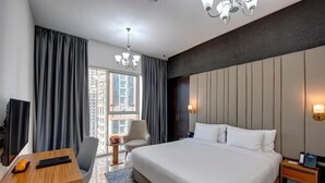 Ett modernt hotellrum med en stor säng, ett skrivbord, en stol, en TV och utsikt över staden.