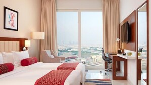 Habitación de hotel con dos camas, un escritorio, un televisor y vistas a la ciudad.