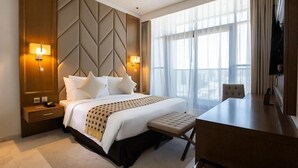 A hotel room with a large bed, bedside lamps, a desk, and a view of the city through large windows. - One Bedroom Apartment in Al Qusais By E R (Dubai)