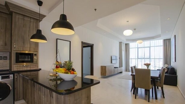 A modern kitchen with a central island, wooden cabinets, and a dining area with a table and chairs. - One Bedroom Apartment in Al Qusais By E R (Dubai)